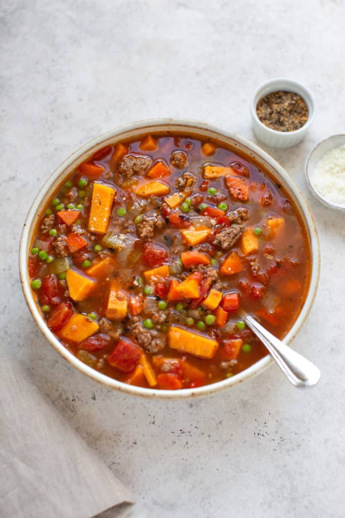 vegetable soup with hamburger in a bowl and spices on the side 