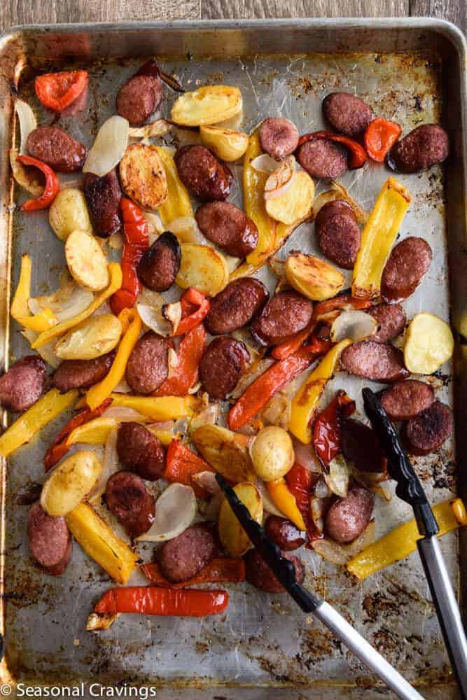 A gluten-free baking sheet with sausages and peppers on it.