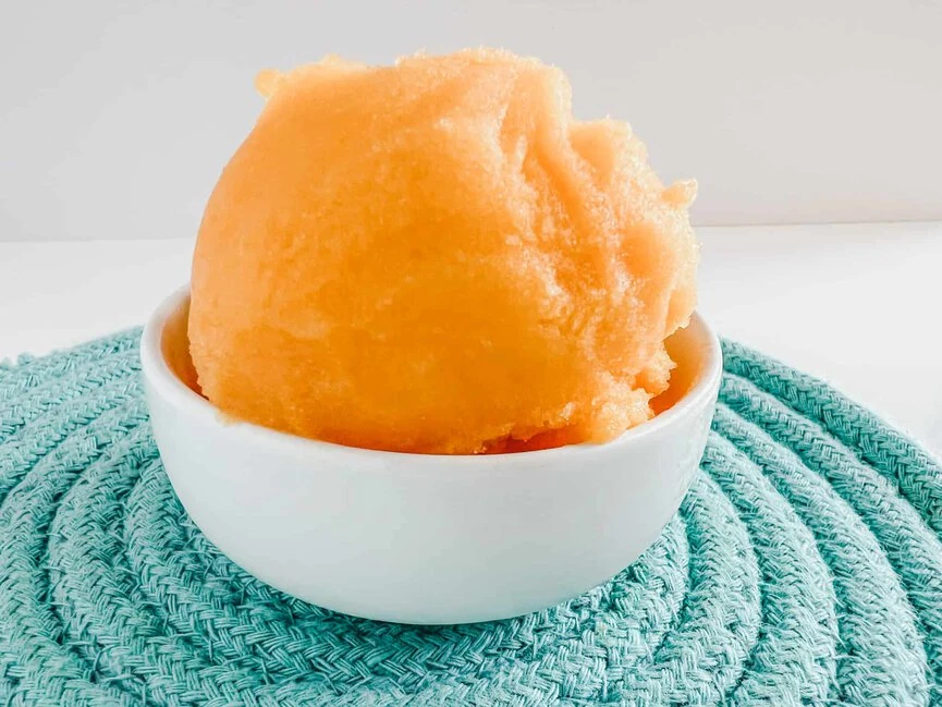 Orange sorbet in a bowl on a blue tablecloth.