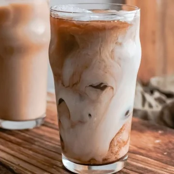 Two glasses of iced coffee adorned on a wooden cutting board accompanied by 28 Copycat Starbucks Drink Recipes.