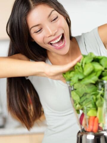 Vegetable smoothie woman making green smoothies with blender home in kitchen. Healthy raw eating lifestyle concept portrait of beautiful young woman preparing drink with spinach, carrots, celery etc.