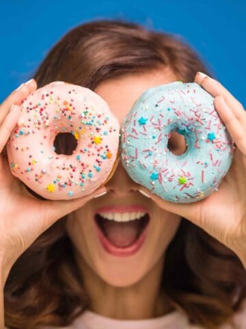 Young woman is holding donuts against her eyes and smiling while
