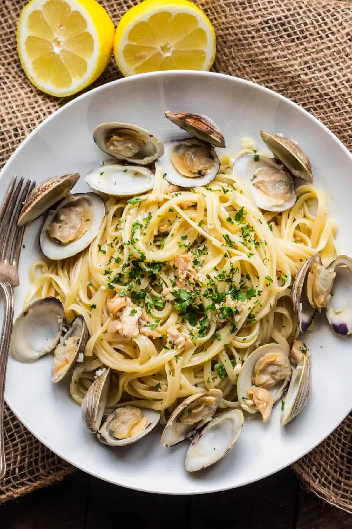 Quick and easy dinner idea: Clams and pasta served on a white plate with lemon wedges.