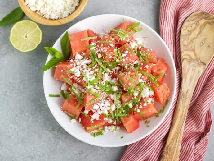 skinny watermelon feta salad in a white bowl with wooden spoon