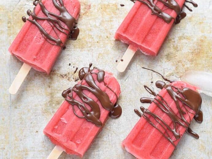Strawberry Popsicles with Chocolate Drizzle on a sheet pan with ice