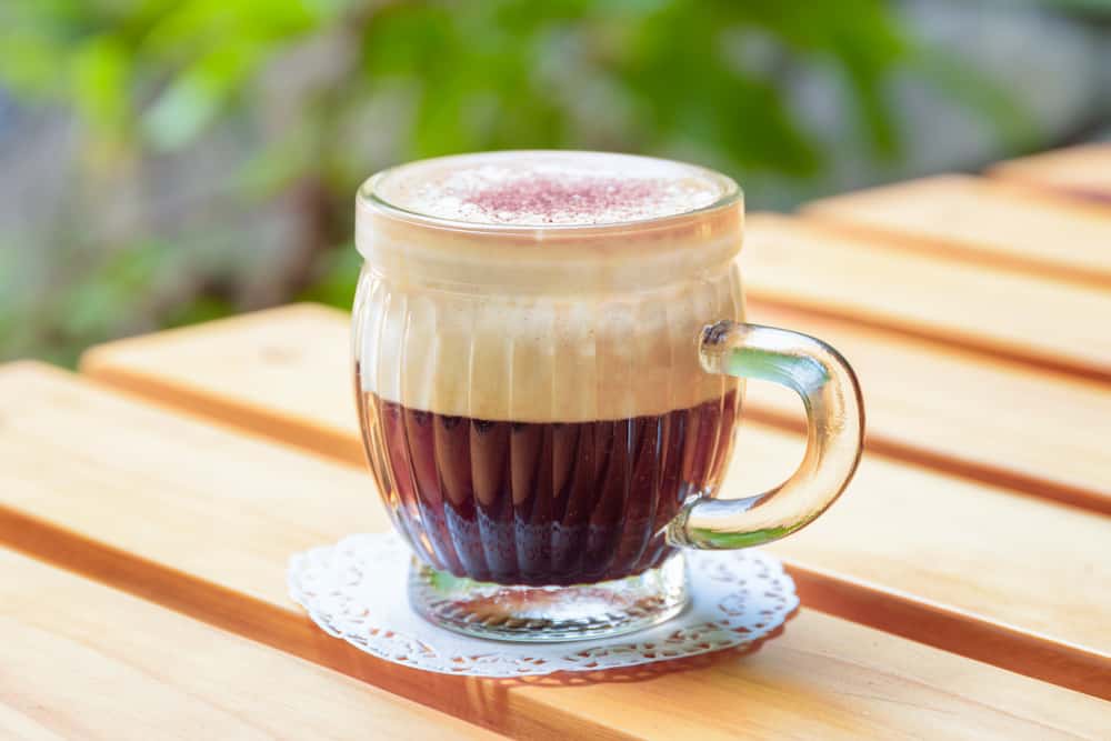 Cup of Vietnamese egg coffee (ca phe trung) on wooden table of street cafe on natural background. Traditional drink in Vietnam.