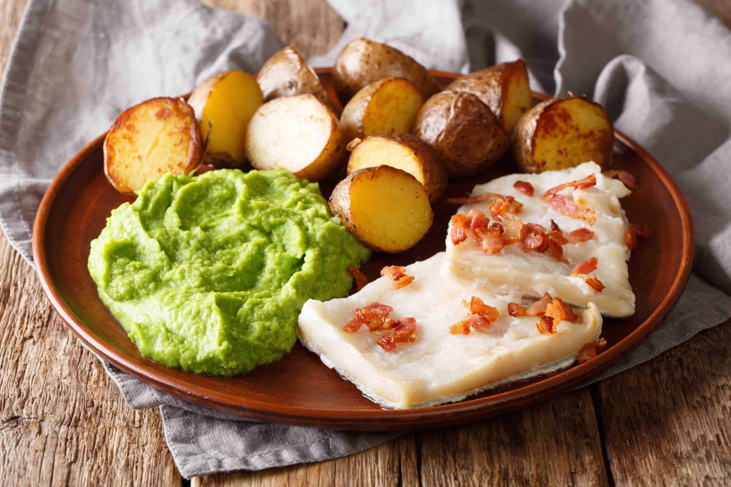 Traditional Scandinavian dish lutefisk served with pea puree, potatoes and bacon close-up on a plate. horizontal