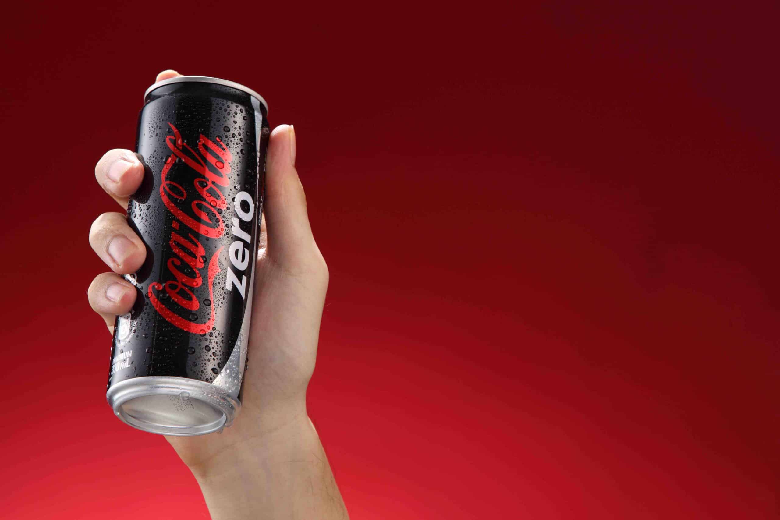  Hand hold a  can Coca-Cola Zero on red  background. Coca Cola drinks are produced and manufactured by The Coca-Cola Company.