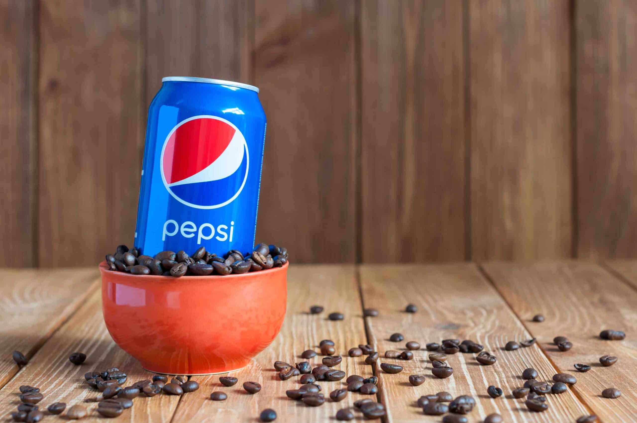 Can of Pepsi cola in a bowl of coffee standing on a dark wooden background with empty space. Pepsi is a carbonated soft drink that is produced and manufactured by PepsiCo. Created and developed in 1893.