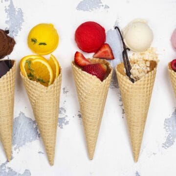Assortment of ice cream flavors, waffle cones and ingredients on white background. Chocolate, orange, strawberry, vanilla and raspberry ice cream