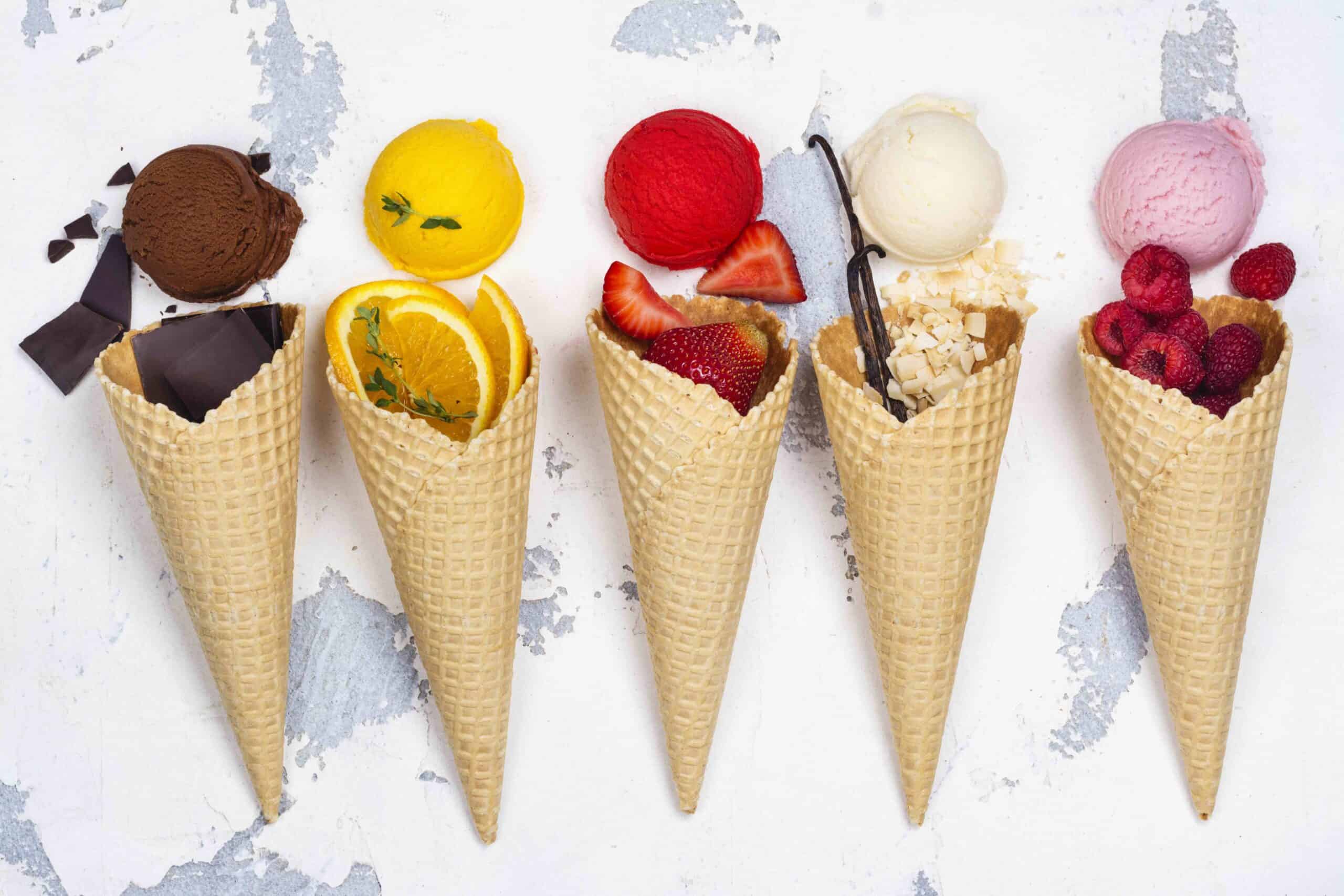 Assortment of ice cream flavors, waffle cones and ingredients on white background. Chocolate, orange, strawberry, vanilla and raspberry ice cream