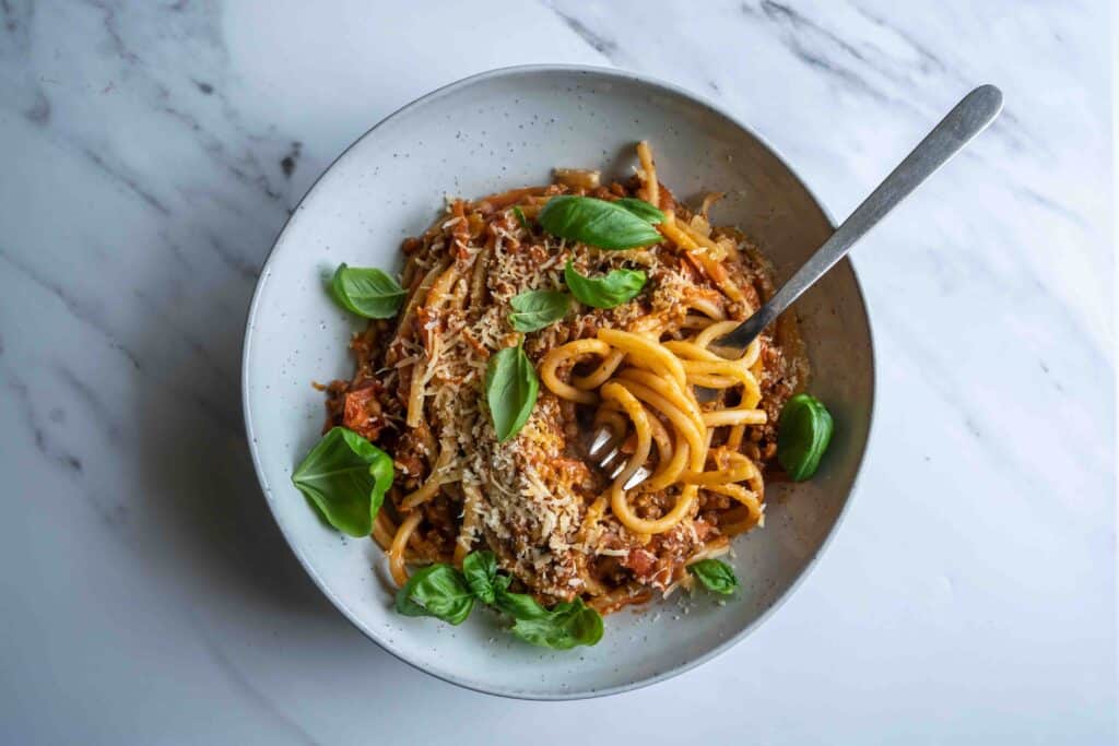 Vegan lentil pasta, bucatini with fresh home made tomato lentil sauce, basil and parmesan cheese on white concrete background with copy space