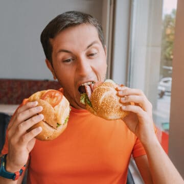 Happy man eating two hamburger or sandwich with an appetite in a fast food cafe.