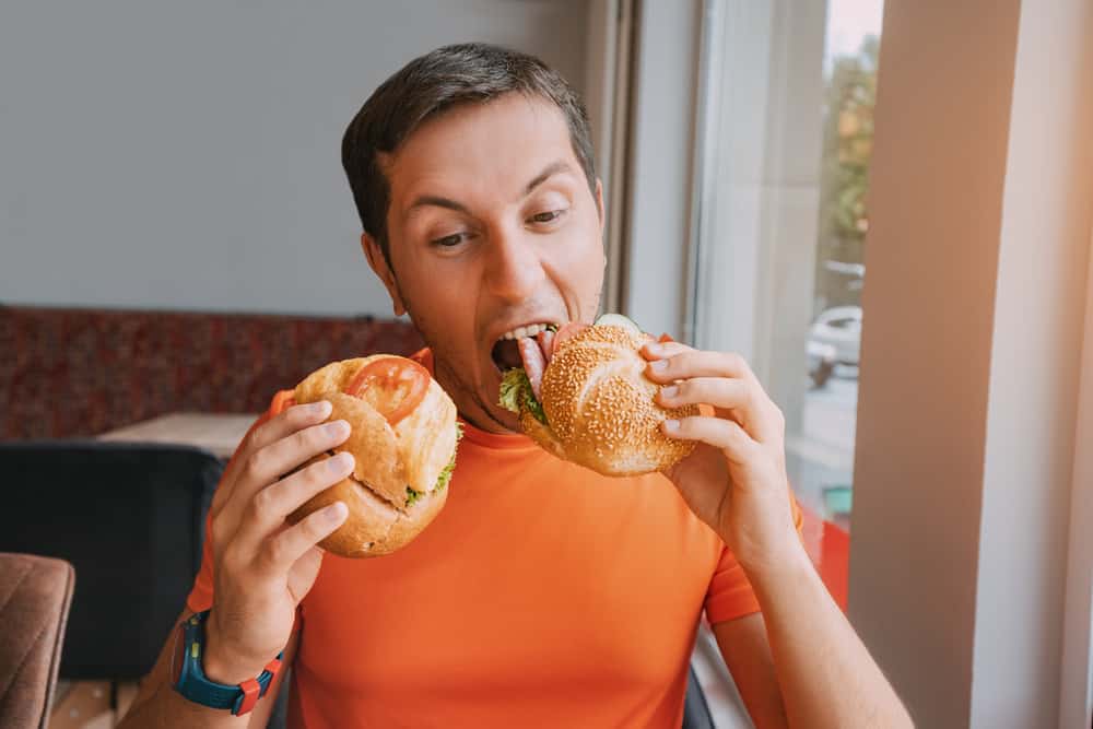 Happy man eating two hamburger or sandwich with an appetite in a fast food cafe.
