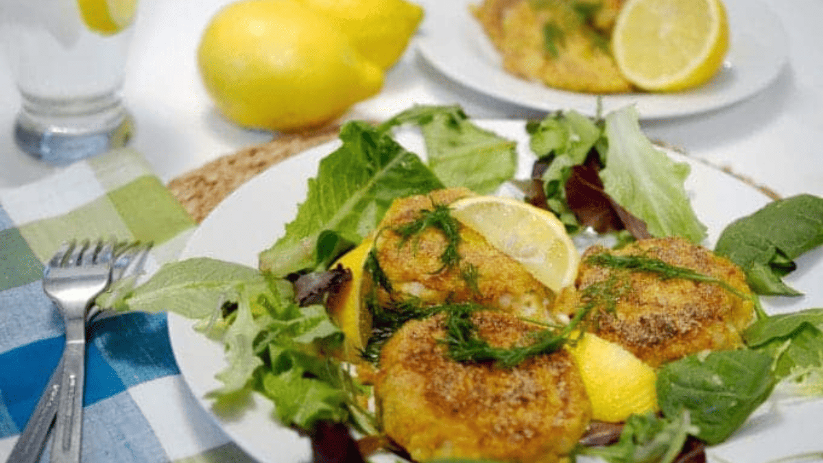 A platter of cod cakes with lemon wedges.
