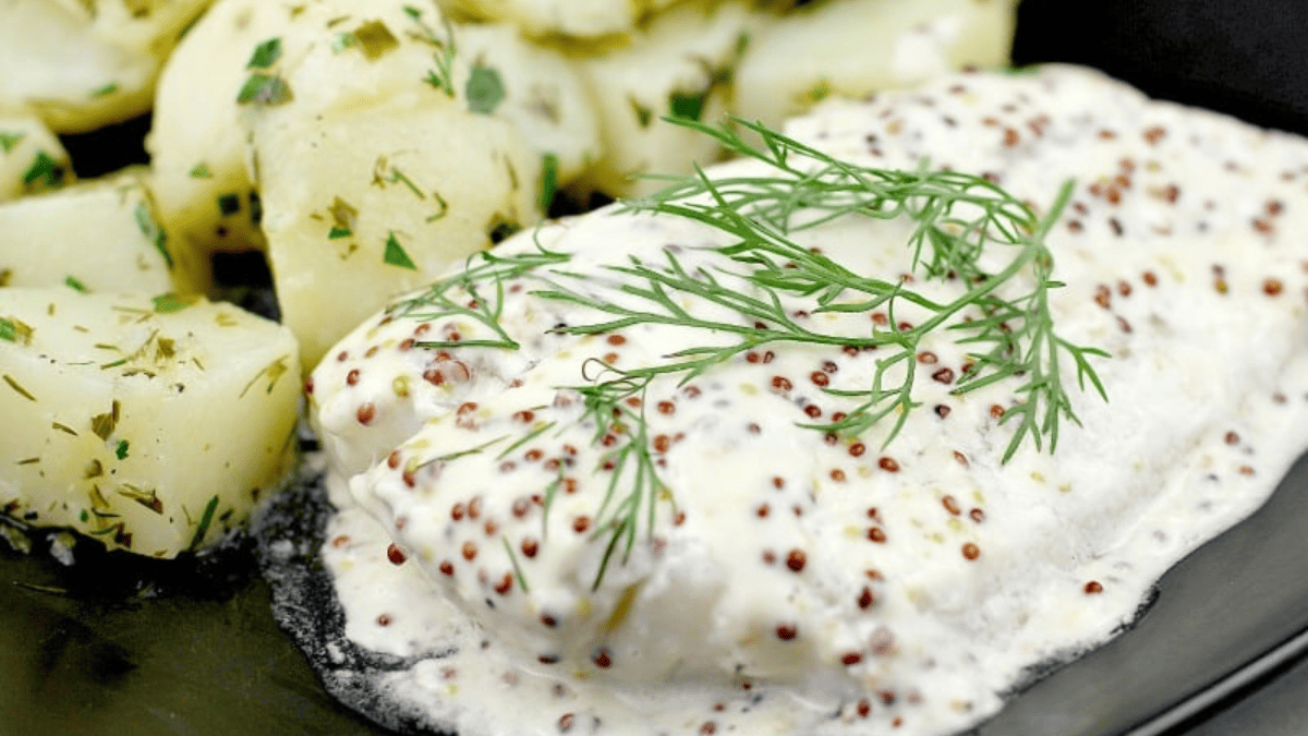 Baked cod with seedy mustard cream with herby potatoes on a plate.
