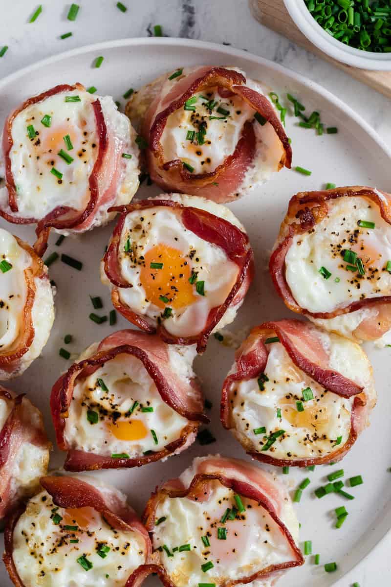 A plate of make-ahead bacon and egg cups, perfectly baked in a muffin pan, is garnished with fresh chopped chives.