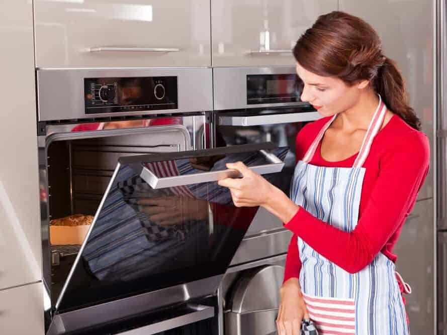 Beautiful young woman checking how her cake is doing in the oven