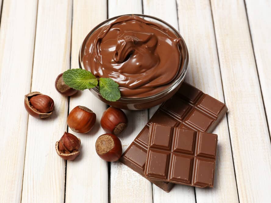 Sweet chocolate hazelnut spread with whole nuts and mint on wooden background