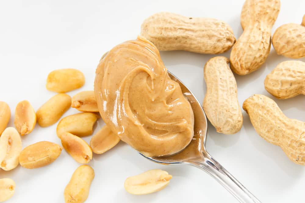 Creamy peanut butter and peanuts against a white tray show healthy foods that are also allergens
