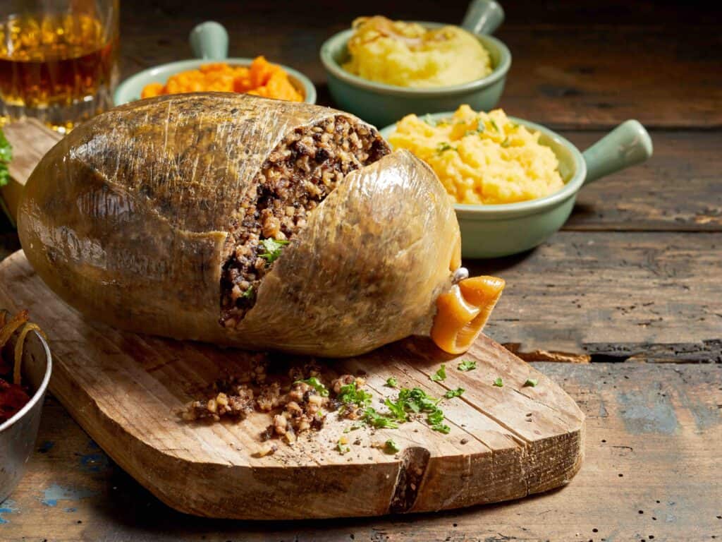 Cooked sliced open haggis and vegetables with mashed turnip, potato and fried onions on a rustic wood table with copy space