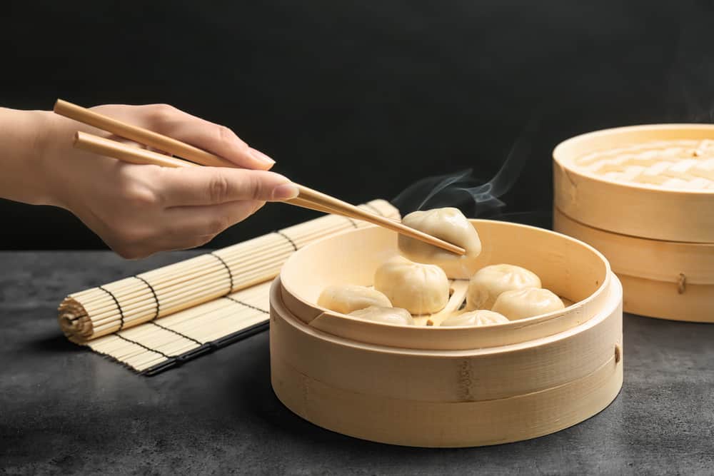 Woman with tasty baozi dumplings in bamboo steamer on table