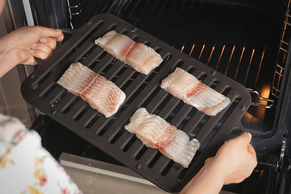 Woman putting broiler pan with fish fillet slices into oven