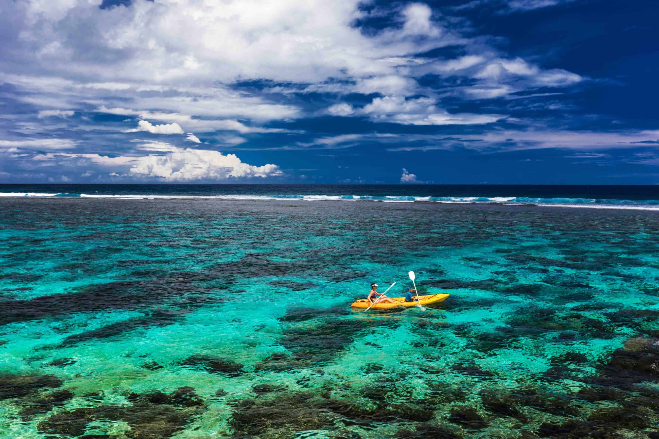 Female and little boy paddling canoe on a lagoon with tropical coral reef