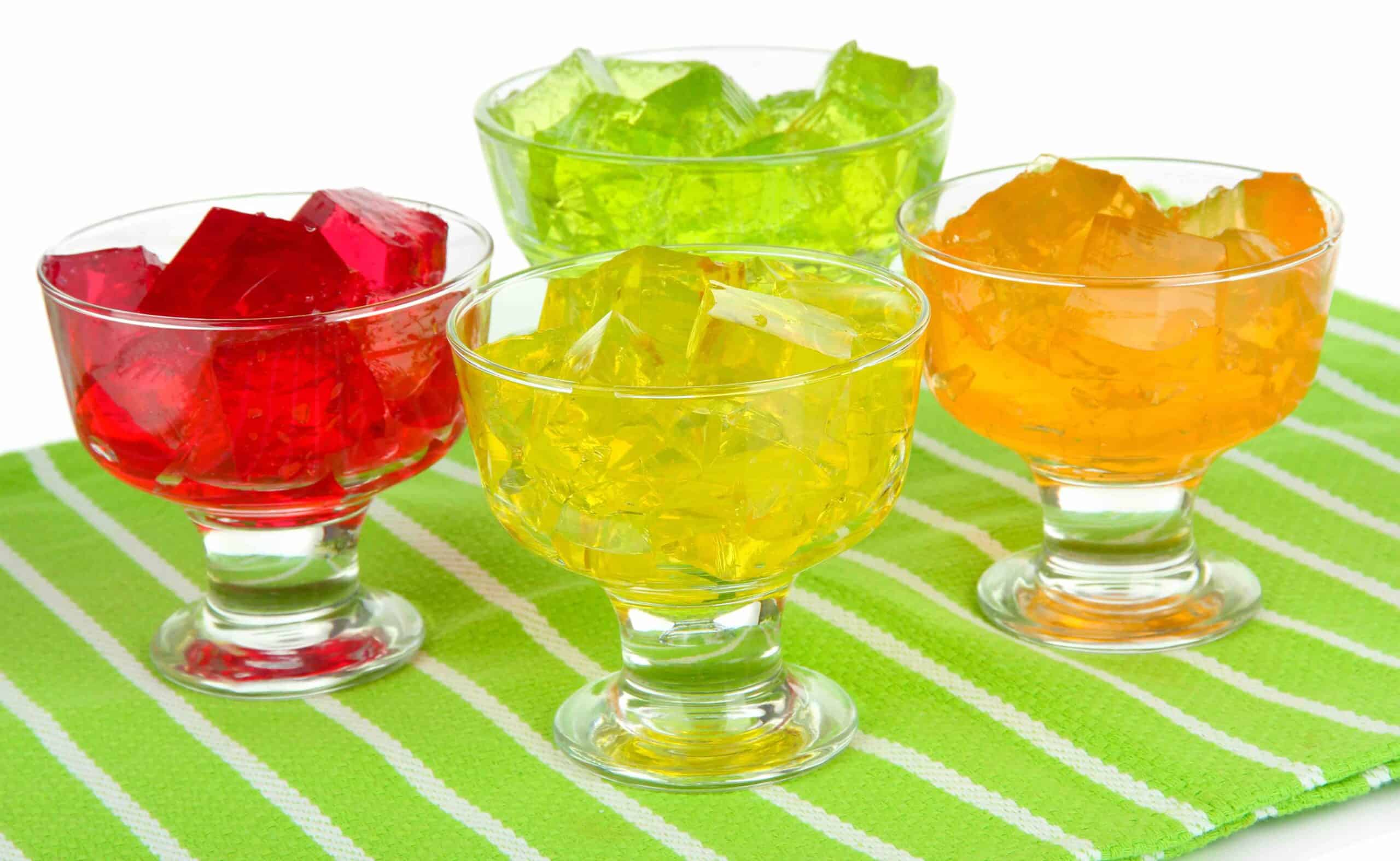 Tasty jelly cubes in bowls on table on white background