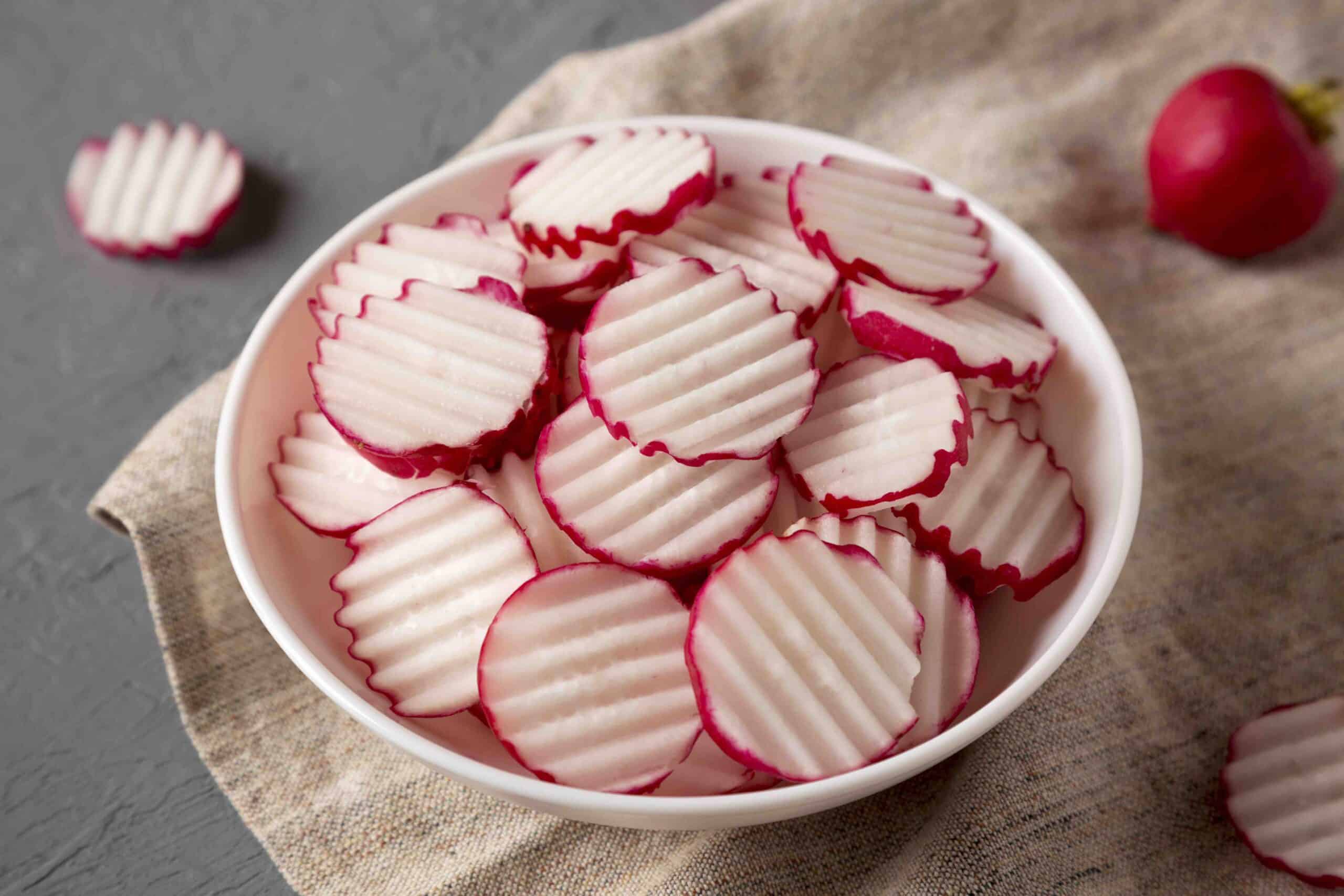 Fresh Radish Chips Slices in a white bowl on a gray background, low angle view. Close-up.