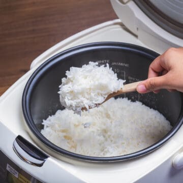 Woman hand is scooping jasmine rice cooking in electric rice cooker with steam. Thai Jasmine rice.