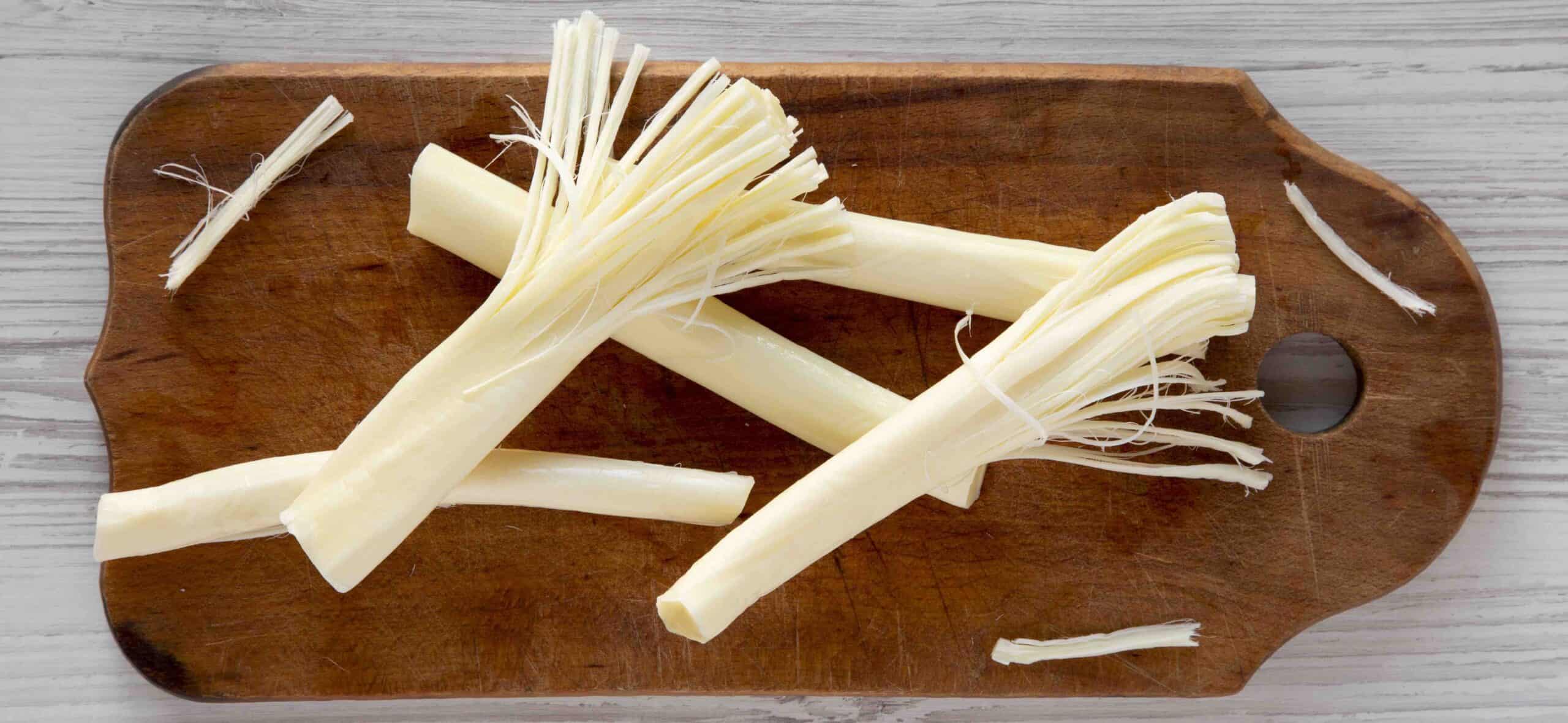 String cheese on rustic wooden board over white wooden surface, top view. Healthy snack. Flat lay, overhead, from above.