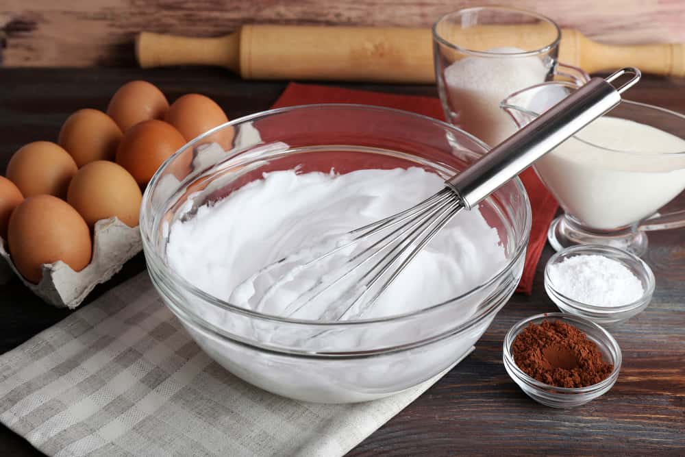 Whipped egg whites for cream and other ingredients on wooden table, closeup