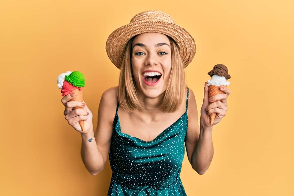 Young caucasian blonde woman eating ice cream cone smiling and