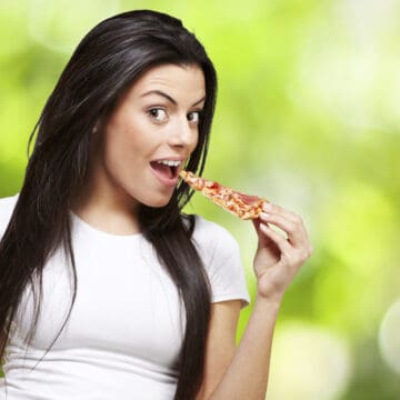 young woman eating a piece of pizza against a nature background