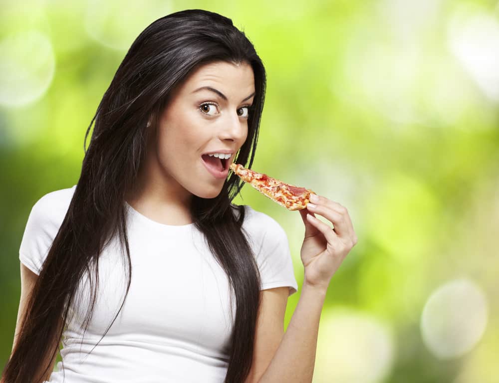 young woman eating a piece of pizza against a nature background