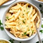 A bowl of gluten-free chicken penne pasta with parmesan cheese and bread.
