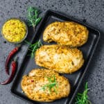30 air fryer chicken recipes featuring three chicken breasts on a black tray seasoned with herbs and spices.