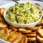 A gluten free appetizer featuring a bowl of broccoli dip accompanied by bread and a fork.