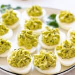 Deviled eggs topped with guacamole and garnished with parsley, a delicious gluten-free appetizer.
