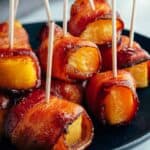 Bacon wrapped peaches with toothpicks on a plate, perfect for serving as one of the 46 gluten-free appetizers.