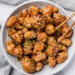 Sesame chicken served in a white bowl with chopsticks, a delicious and gluten-free appetizer option.