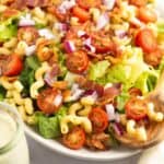 A gluten-free pasta salad with bacon, tomatoes and dressing on a white plate.