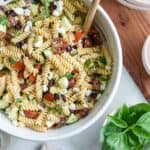 Gluten-free Greek pasta salad in a white bowl with a wooden spoon.