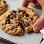 A hand removing a chocolate chip cookie from a baking sheet containing 40 Gluten Free Cookies.