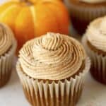 Gluten-free and dairy-free pumpkin cupcakes topped with delightful icing and miniature pumpkins.