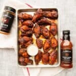 30 delectable BBQ chicken wings on a baking sheet, served with a bottle of sauce.