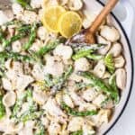 Gluten-free chicken and asparagus pasta in a skillet with lemon wedges.