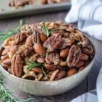 Healthy snack of roasted pecans in a bowl with rosemary sprigs.