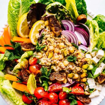 A white bowl filled with a gluten-free salad with tomatoes, lettuce and figs.